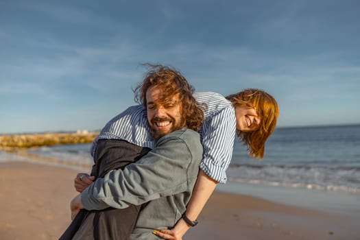 Smilng couple fool around while walking along the beach on sunny windy day. High quality photo