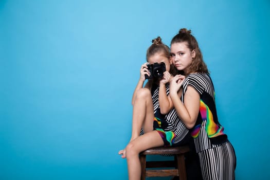 Two fashionable girls with a camera on a blue background