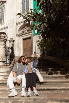 Couple in love sitting stairs on old city street and making selfie on phone. High quality photo