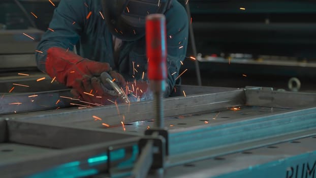 Man in mask works with welding metal structures at factory. Creative. Welder in equipment works at industrial plant. Worker with welding and welding sparks from metal.