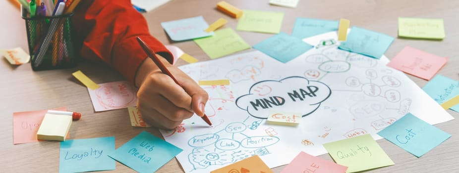 Professional startup group share creative marketing idea by using mind map. Young skilled business people brainstorm business plan while writing sticky notes. Focus on hand. Closeup. Variegated.