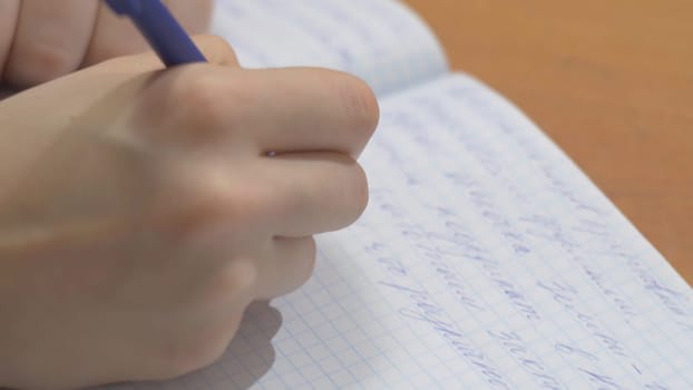 Female hands with pen writing on notebook. Close up of woman's hands writing in spiral notepad placed on wooden desktop with various items f