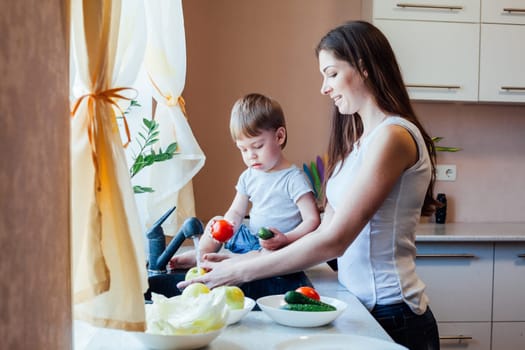 kitchen little son helps mom wash fruits and vegetables in the sink