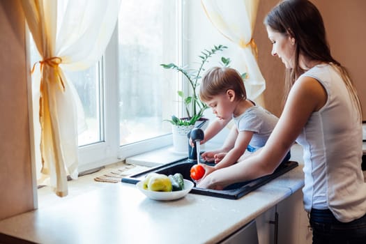 mother and young son wash their vegetables in the kitchen sink