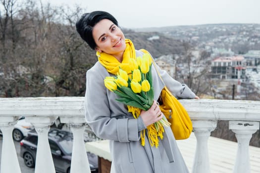 Portrait of brunette in coats with yellow tulips on the street