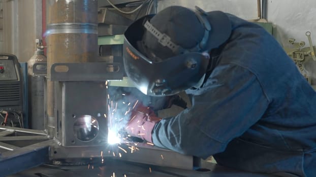 Welder in workshop repairs structure with sparks. Creative. Work of welder in industrial production. Welder in mask with welding sparks repairs structure in production.