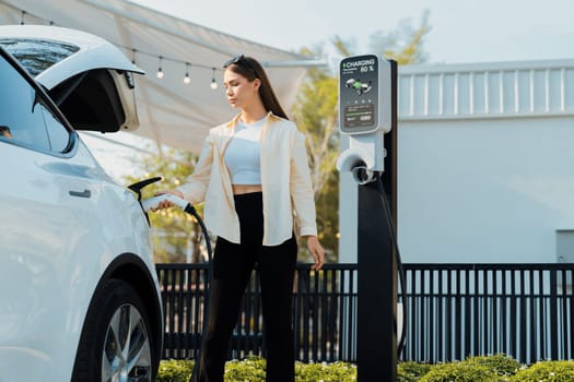 Young woman put EV charger to recharge electric car's battery from charging station. Alternative energy and rechargeable EV car for sustainable environmental friendly travel concept. Expedient