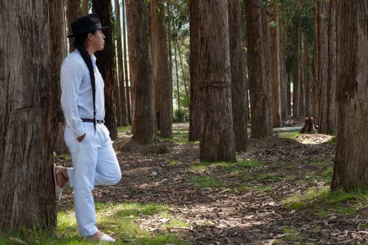 horizontal photo with copyspace of an ecuadorian indian with white clothes and a long braid to the waist with a black hat looking at the horizon full of trees. hair day. High quality photo
