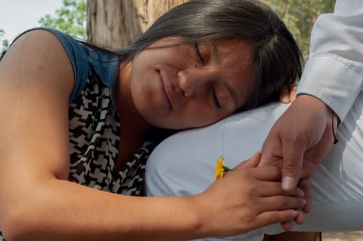 latin girl in love resting her head on her beloved's leg with her eyes closed while holding hands and holding a flower of the field between her hands. valentine's day. High quality photo