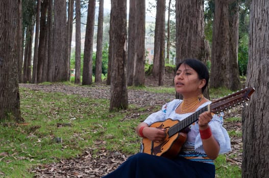 copy space of an indigenous girl from ecuador sitting singing and playing a mandolin in the middle of the forest . music day . High quality photo