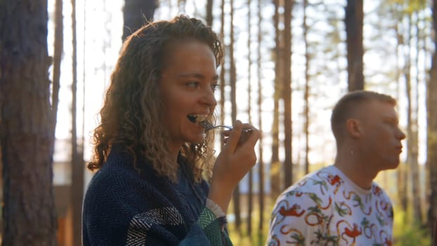 Group of friends eats vegetables at grill in nature. Stock footage. Beautiful friends have fun chatting at barbecue in forest. Fun vacation with friends in forest on sunny summer day.