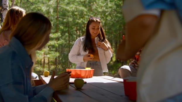 Young people play beer pong. Stock footage. Game for group of friends with glasses of alcohol and ping pong ball. Friends play beer pong in nature in summer.