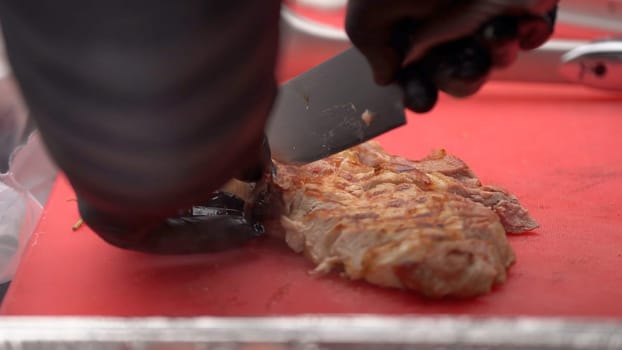 Chef in black gloves cuts juicy meat steak on the wood board with the knife, close-up. Delicious, juicy, freshly cooked meat steaks cook cuts on the cutting board. Juice from the steaks remains on the board.