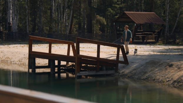 Man walks with dog at pier of lake. Stock footage. Man brought dog to pier by pond in forest. Man walks with dog at recreation center by lake in summer.