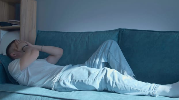 Tired young man lies down on sofa. Media. Young man lies down on sofa after hard day's work. Emotionally tired young man lie down on sofa.