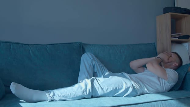 Tired young man lies down on sofa. Media. Young man lies down on sofa after hard day's work. Emotionally tired young man lie down on sofa.