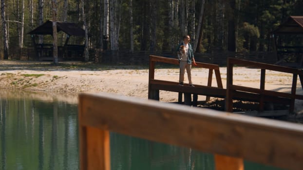 Man with dog on lake pier. Stock footage. Beautiful lake with pier and man holding dog in hands. Relaxing with dog on summer lake in forest on sunny day.