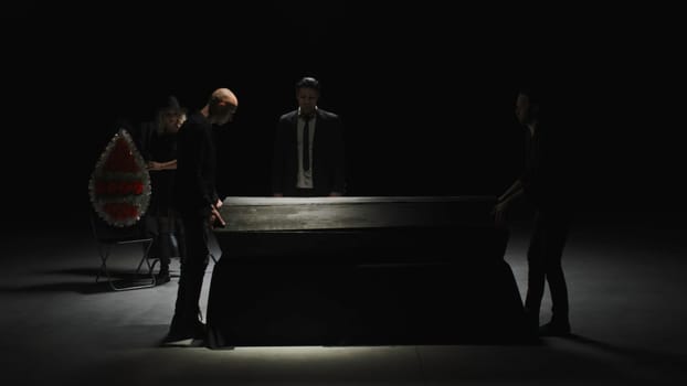 Theatrical production in dark room. Stock footage. Funeral on theater stage with actors. Theatrical staging of funeral in dark room with actors and props.