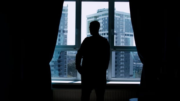 Silhouette of a business man talking on a mobile phone on the background of a window and city. Media. Successful confident businessman standing at home by the window