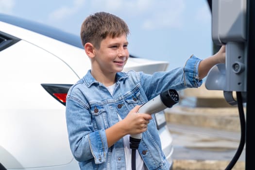 Little boy recharging eco-friendly electric car from EV charging station. EV car road trip travel concept for alternative transportation powered by clean renewable and sustainable energy. Perpetual