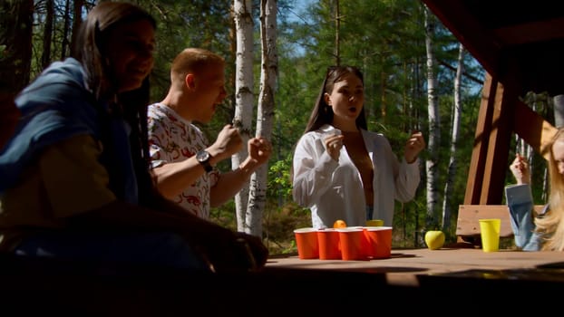 Friends have fun playing beer pong. Stock footage. Fun game with friends and alcohol in nature in summer. Friends actively play beer pong in nature on sunny day.