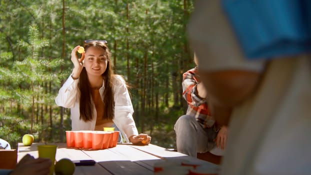 Young woman playing beer pong. Stock footage. Beautiful woman throws ball into glass of beer. Fun game for friends with alcohol and ping pong in nature in summer.