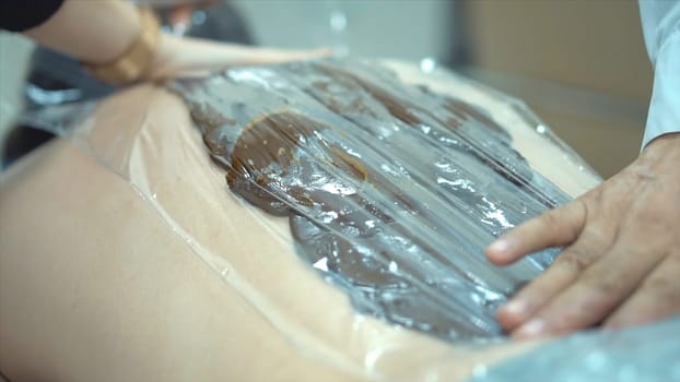 Close-up of man's back during chocolate body wrap treatment. Rest in spa