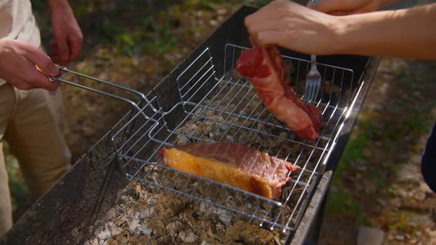 Close-up of man cooking juicy pieces of meat on grill. Stock footage. Man cooks two delicious pieces of red meat on coals. Grilling meat outdoors in summer.