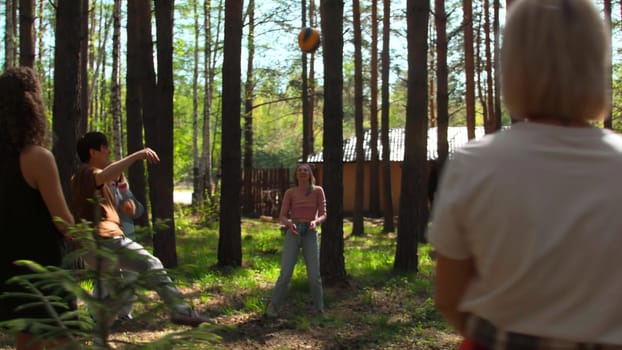 Group of friends is having fun playing volleyball. Stock footage. Friends are playing volleyball in forest clearing. Friends in circle play volleyball in forest on sunny summer day.