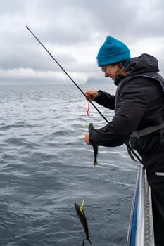 A happy female angler displays her fishing success in the stunning Norwegian sea, enjoying her favorite hobby. For her, the serene pastime of fishing brings happiness and a sense of achievement.