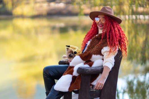 Autumn lake woman dog. She sits by a pond on a wooden pier in autumn and admires nature, holding a Yorkshire terrier in her hands. The concept of tourism, weekends outside the city