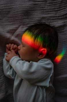 Close-up portrait of a newborn boy with a prism beam on his face. Rainbow