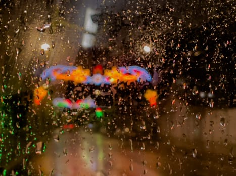 Rain bokeh road lights. Abstract shot of evening city traffic bokeh. Multicolored lights of the evening city and passing cars through a wet rainy window