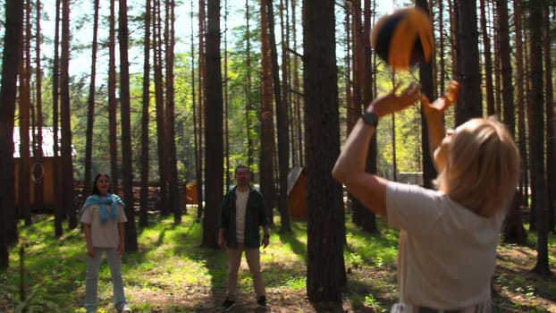 People at recreation center play volleyball. Stock footage. Group of people are playing volleyball in forest on sunny summer day. Tourists play volleyball in circle in forest.