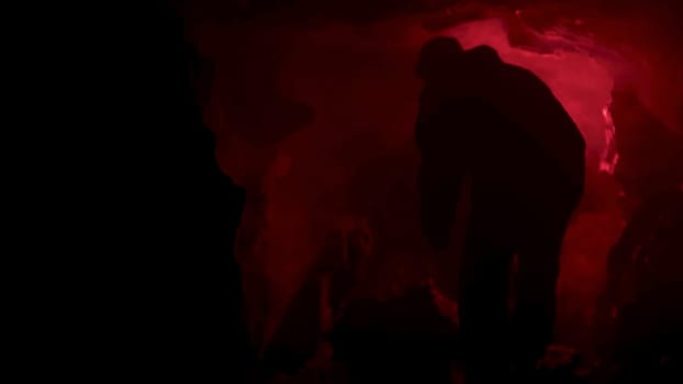 red signal flare burning inside dark natural cave making shadows on cave walls. Man got lost inside grotto and looking for help at night.