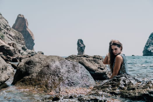 Woman travel sea. Young Happy woman in a long red dress posing on a beach near the sea on background of volcanic rocks, like in Iceland, sharing travel adventure journey