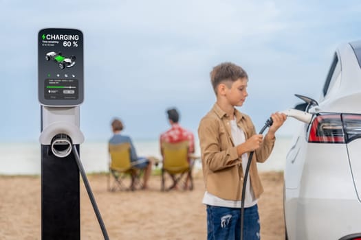Family vacation trip traveling by the beach with electric car, little boy recharge EV car while his family enjoy seascape beach. Family trip with alternative energy and eco-friendly car. Perpetual