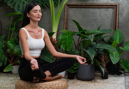 Young woman doing morning yoga and meditation in natural garden with plant leaf, enjoying the solitude and practicing meditative poses. Mindfulness activity and healthy mind lifestyle. Blithe