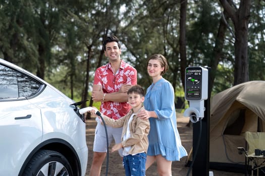 Outdoor adventure and family vacation camping in nature travel by eco friendly car for sustainable future. Lovely family recharge EV car with EV charging station in campsite. Perpetual