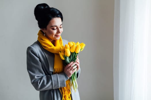 girl with yellow tulips stands at the window in the room 1