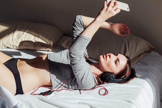 a girl takes pictures himself on a smartphone on the bed with headphones