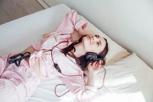 girl in pink Pajamas lying on the bed and listens to music