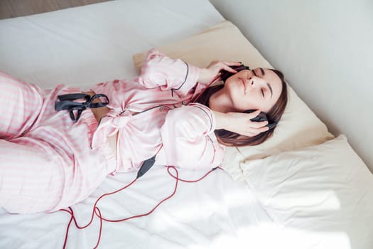 girl in pink Pajamas lying on the bed and listens to music