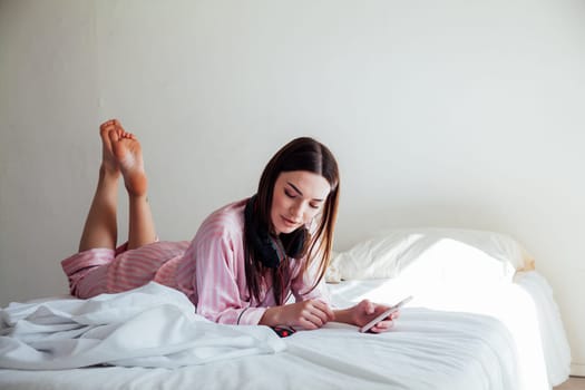 girl in pink Pajamas lying on the bed and listens to music