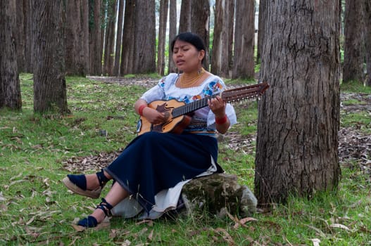 young latin american girl playing a mandolin in the forest while singing with a great feeling on her face. music day. High quality photo