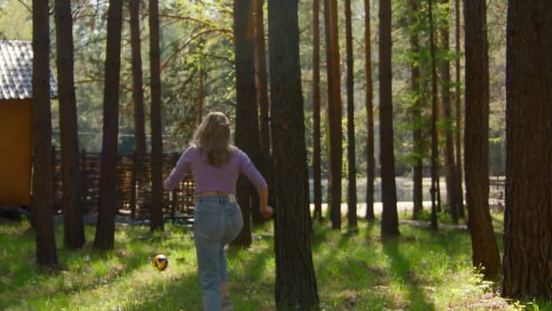 Young woman runs after ball in park. Stock footage. Woman runs after volleyball in sunny park. Beautiful young woman is having fun running after ball in woods.