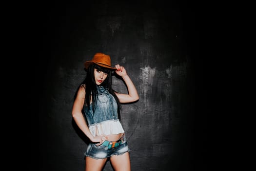 beautiful sexy girl in cowboy hat and denim waistcoat on a black background