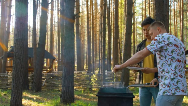 Men put barbecue on plate in nature. Stock footage. Men cooked sausages on grill in forest on sunny summer day. Men put barbecue meat on plate in nature.