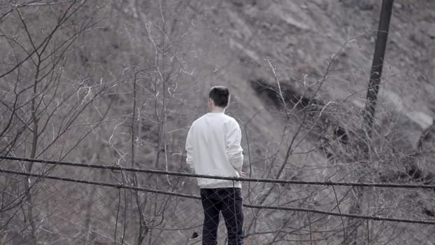 Rear view of a man standing at the edge of an autumn grey dirty slope. Stock footage. Young man looking thoughtful