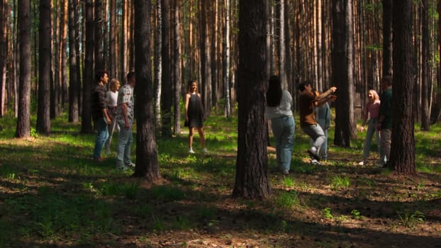 Group of people playing volleyball in forest. Stock footage. People play volleyball on hiking trip in forest. Group of tourists playing ball in forest on sunny summer day.